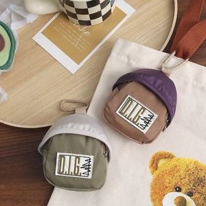 Close-up of mini backpack coin purses in olive and purple with D.L.G patches and carabiners