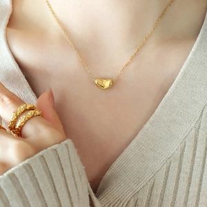 Detail der goldenen Bohnen-Halskette mit texturiertem Ring am Modell bei sanftem Licht