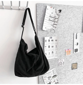 Detail view of a black corduroy tote bag hanging on a hook with artistic room decor