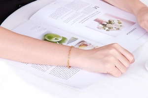 Detail of gold titanium steel bracelet with hammered texture worn by a model over a magazine