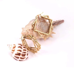 Detail of geometric multi-layer gold square earrings on natural seashells with a white background