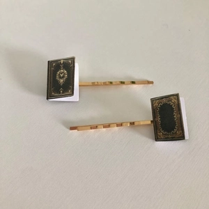 Detailed view of gold hairpins featuring miniature vintage black book charms for book lovers