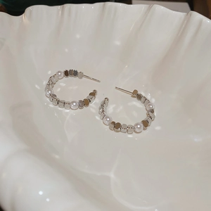 Detailed macro shot of vintage silver C-shaped earrings with pearls on a shell dish