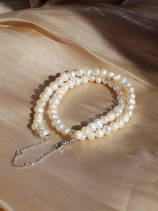 Macro shot of white freshwater pearls with silver lobster clasp on gold silk fabric