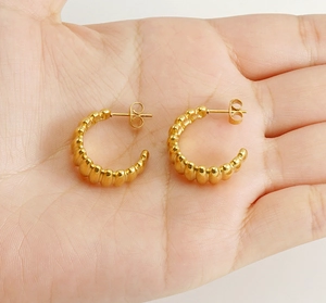 Détail de boucles d'oreilles créoles C dorées texturées présentées sur une main pour l'échelle