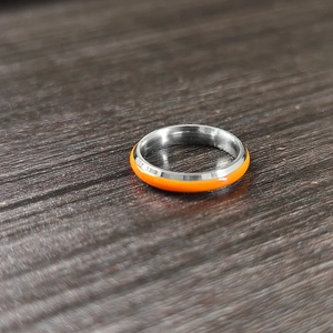 Close-up of minimalist silver stainless steel ring with vibrant orange enamel coating