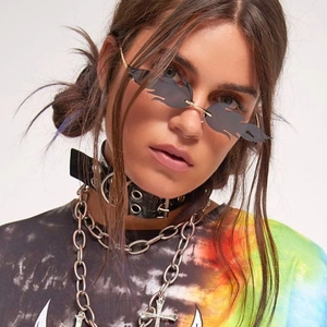 Close-up of flame-shaped rimless sunglasses with punk style layered metal necklaces