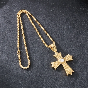 Détail d'un pendentif croix dorée avec gemme claire sur une chaîne vénitienne homme