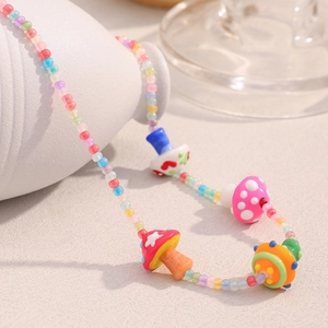 Gros plan d'un collier de perles colorées avec breloques champignon et planète dorées