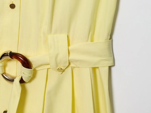 Detail of yellow midi dress featuring tortoise shell belt buckle and gold metal button