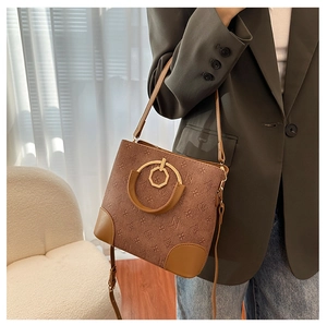 Detail of a brown bucket bag with embossed vintage patterns and gold circular metal buckle