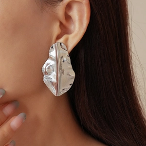 Macro view of silver-tone leaf earrings with irregular textured metallic finish