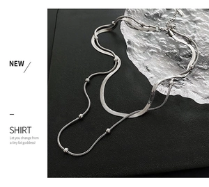 Detail of silver double-layered snake chain and beaded necklace on a black surface