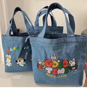 Detail of embroidered cartoon patterns on blue denim tote bags with school text