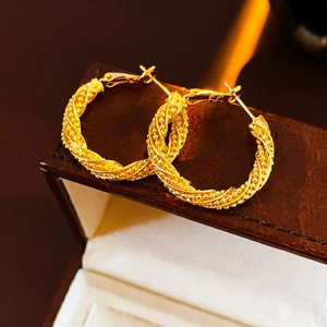 Macro shot of gold twisted hoop earrings showing refined texture on a brown leather box