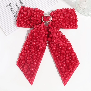Detailed view of a red ribbon bow hair clip with faux pearls and a large center gemstone