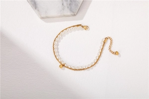 Detailed view of double-layer bracelet with white pearls and gold chain on marble background