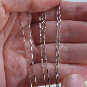 Detail of 1.0mm 925 sterling silver twisted link chain held in hand for scale