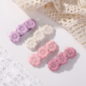 Close-up of four floral embroidery hair clips in purple, cream, and pink shades