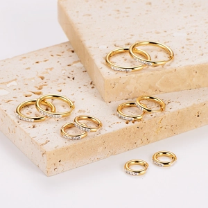 Golden round hoop earrings with clear crystals on travertine stone display stands