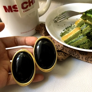 Close-up of vintage oval red stud earrings with gold trim held in hand in a cafe setting