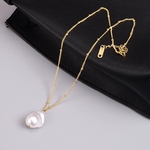 Detail of gold chain with baroque pearl pendant and K18 hallmark tag on leather surface