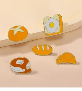 Détail de cinq broches en émail en forme de croissants et crêpes sur fond chaud