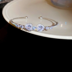 Detailed view of silver zircon open heart bracelet resting on a beige ceramic plate