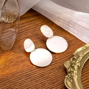 Detail view of round enamel earrings in cream white with gold edges on a wooden table