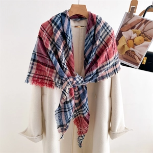 Detail of red and blue plaid scarf with fringes styled on a beige coat over a wooden hanger