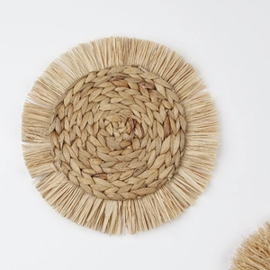 Close-up of handmade woven round table mat with decorative fringe trim and natural fibers