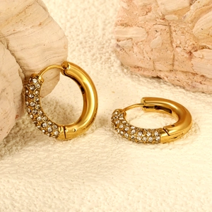 Elegant gold hoop earrings with sparkling clear crystals on a textured stone surface