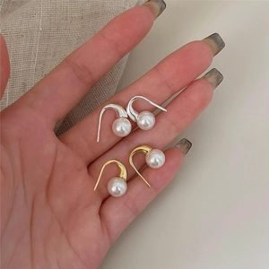 Macro detail of gold and silver pearl drop earrings held in hand for scale and texture