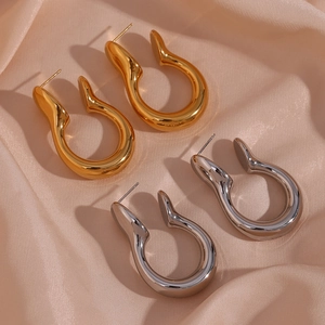 Detail of chunky gold and silver U-shaped hoop earrings on soft pink satin fabric