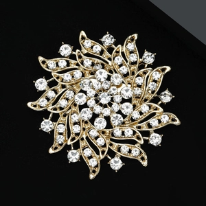 Gros plan d'une broche fleur dorée évidée avec des strass brillants sur fond noir