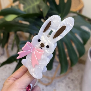 Cute white bunny hair claw clip with pink bow made of acetate held against green plants
