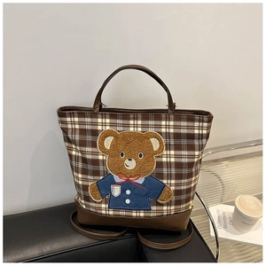 Detail of checkered tote bag with embroidered teddy bear on a stylish leather background