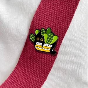 Cartoon black cat in a cactus plant pot enamel pin badge on a red fabric strap