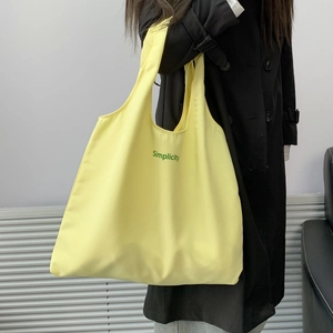Detail of a large yellow canvas tote bag with Simplicity lettering on a model