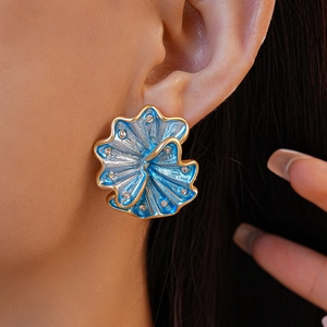 Close-up of blue enamel flower stud earrings with gold trim and rhinestones on model