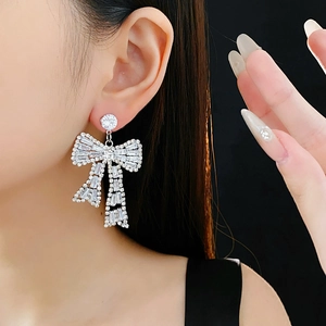 Detail of silver bow earrings with sparkling cubic zirconia on model with black background