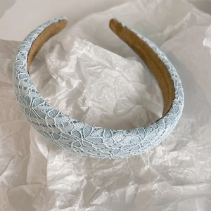 Close-up of a wide light blue lace headband with delicate floral texture on white background