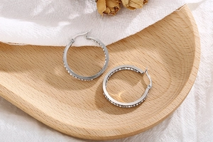 Detailed view of silver diamond hoop earrings on a wooden tray with a minimalist backdrop