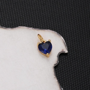 Detailed view of a gold-plated heart pendant with a blue zircon inlay on black texture