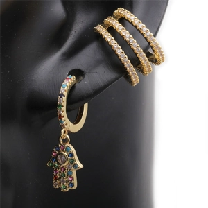Close-up of golden triple-layered ear cuff and Hamsa hand earring with colored stones