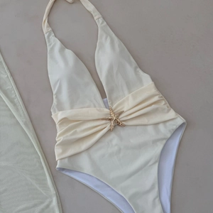 Close-up of beige deep V swimsuit featuring a golden starfish buckle and pleated waist