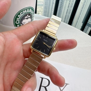 Close-up of a gold square quartz watch with black dial and metal chain strap held by hand