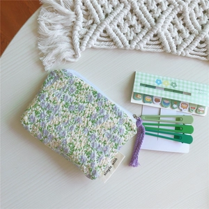 Détail d'une pochette en tissu à fleurs avec pompon violet et fermeture éclair blanche