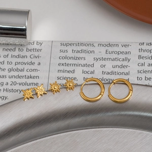 Golden stainless steel earring set featuring star studs and hoops on a metallic surface