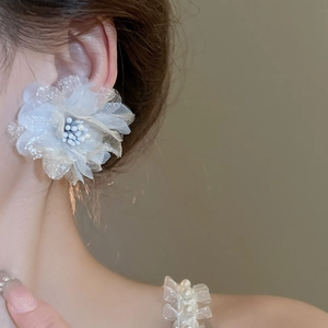 Detail of white mesh lace flower earring with pearl center shown on a model's ear